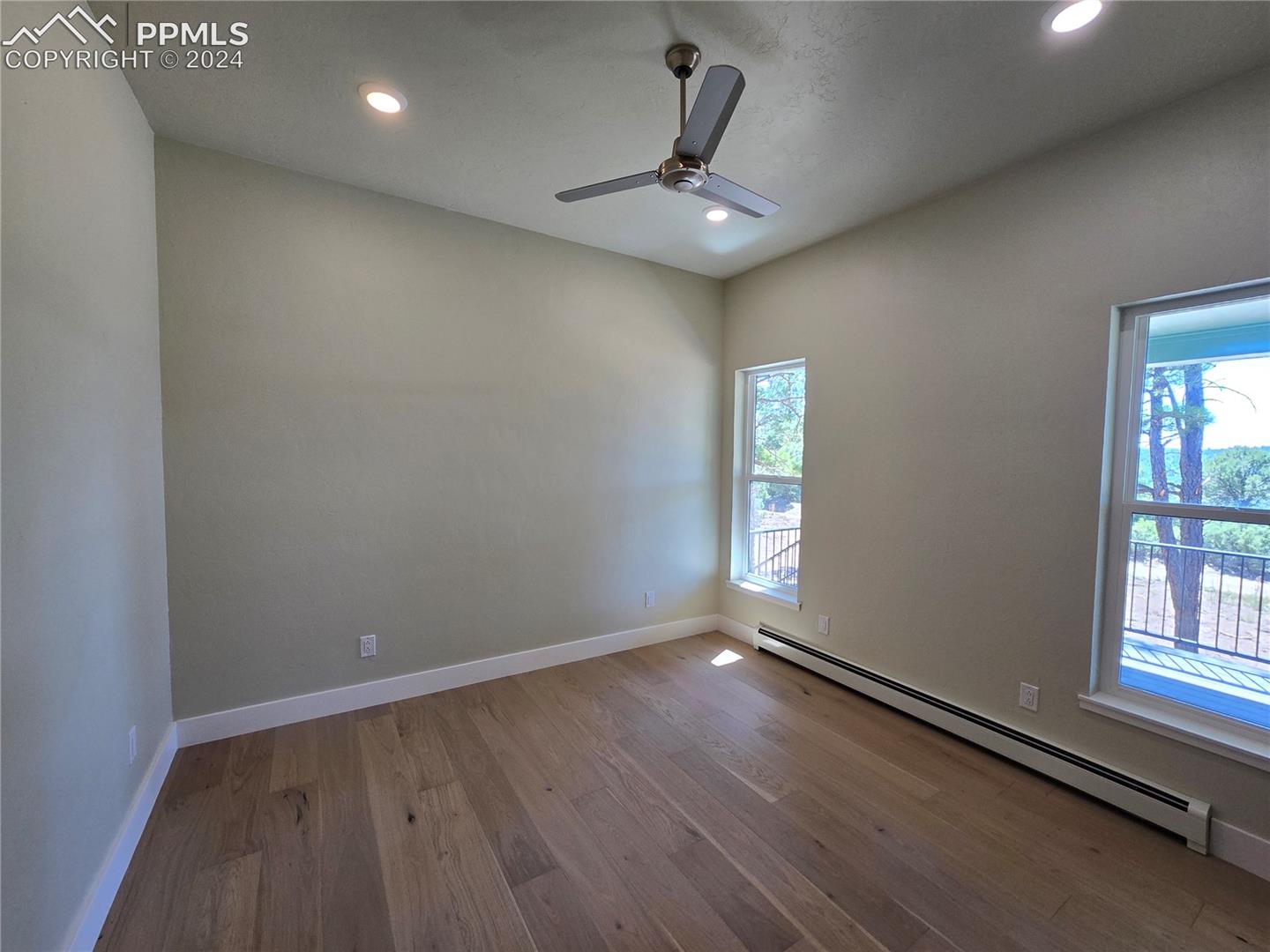 Primary bedroom with a baseboard heating unit, ceiling fan, and light hardwood / wood-style floors