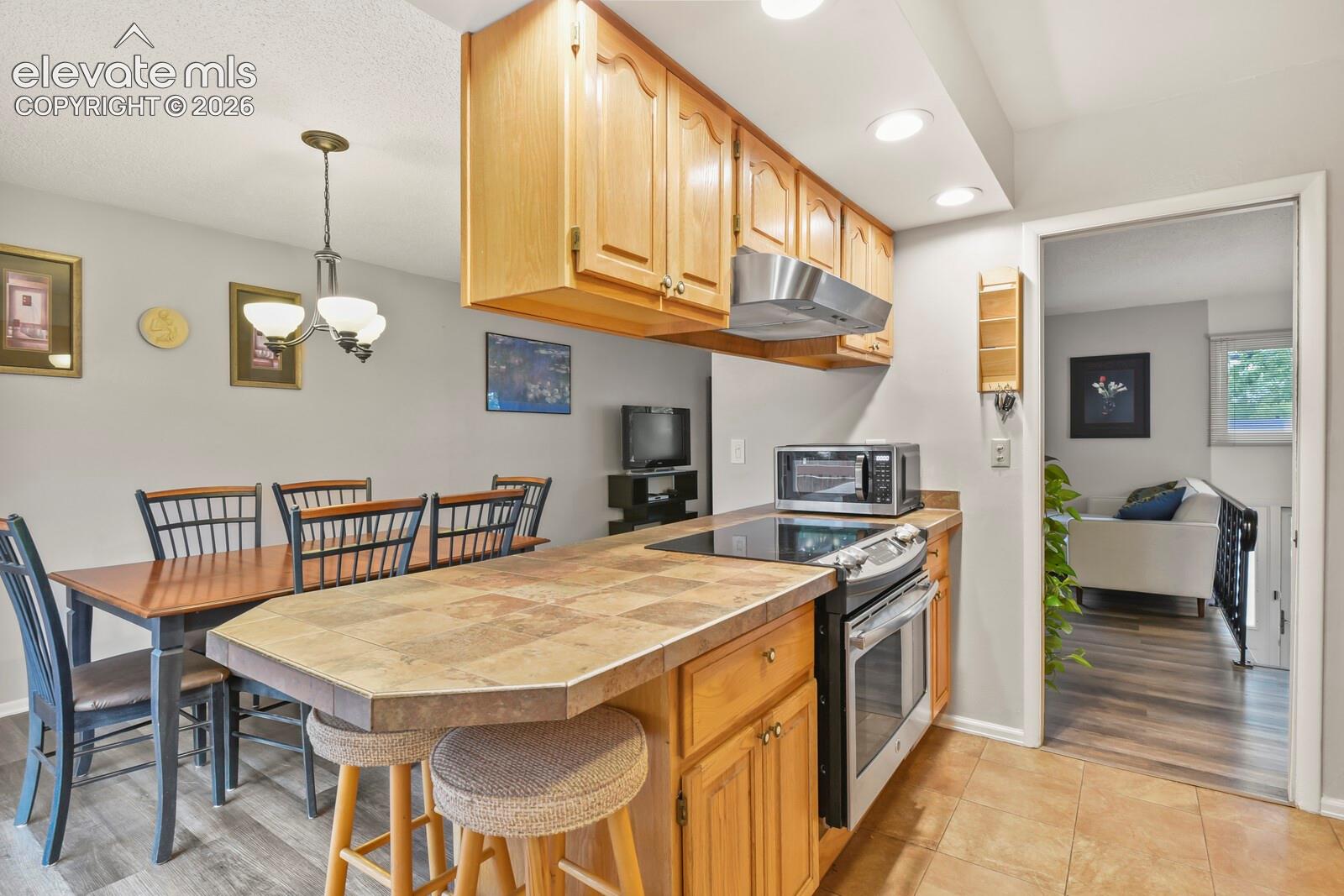 Kitchen featuring wood-finish cabinetry, stainless steel appliances, and a tiled countertop with a breakfast bar