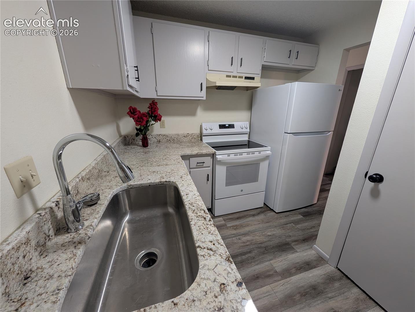 Kitchen featuring a stainless steel sink, chrome gooseneck faucet, light granite-look countertops, white cabinetry, and wood-finish flooring