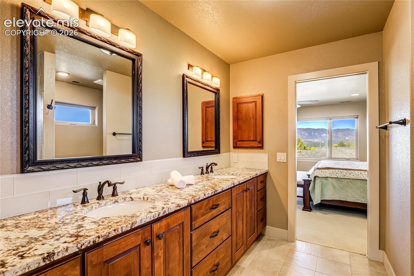 The extended granite-topped vanity offers generous counter space + abundant cabinetry, with warm wood finishes and thoughtfully selected fixtures continuing the home's commitment to beauty + everyday function.