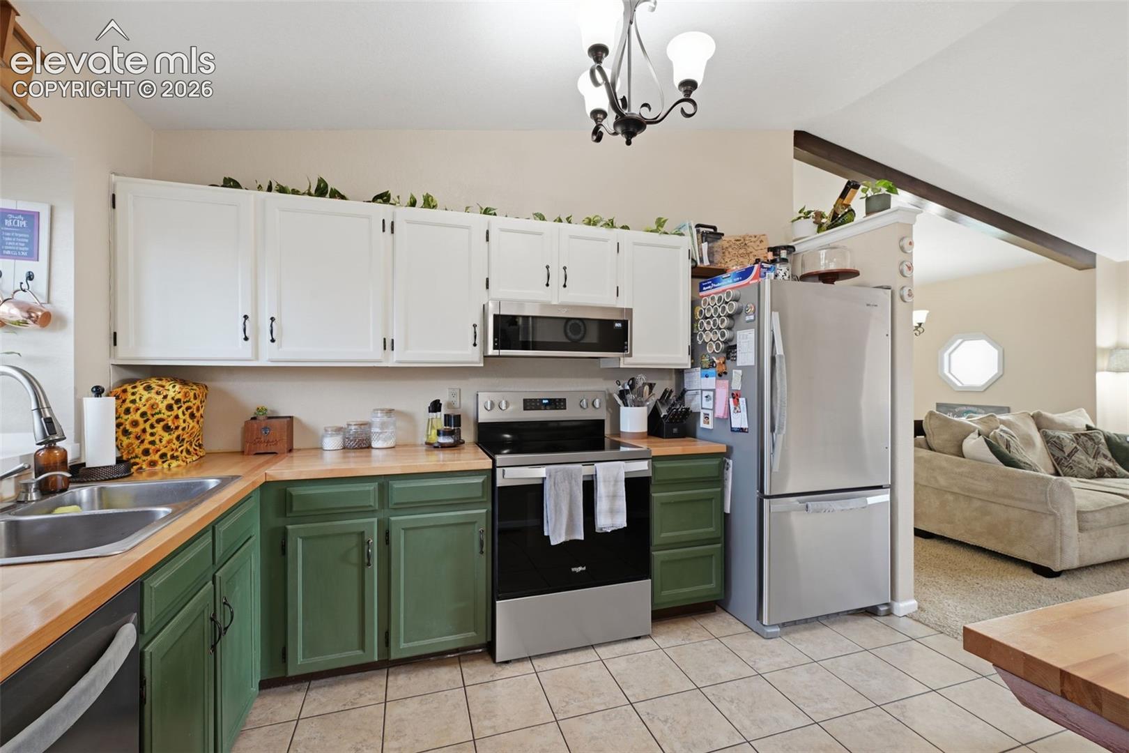 Kitchen featuring two-tone cabinetry with white upper and green lower cabinets, butcher block countertops, stainless steel appliances, and tiled flooring
