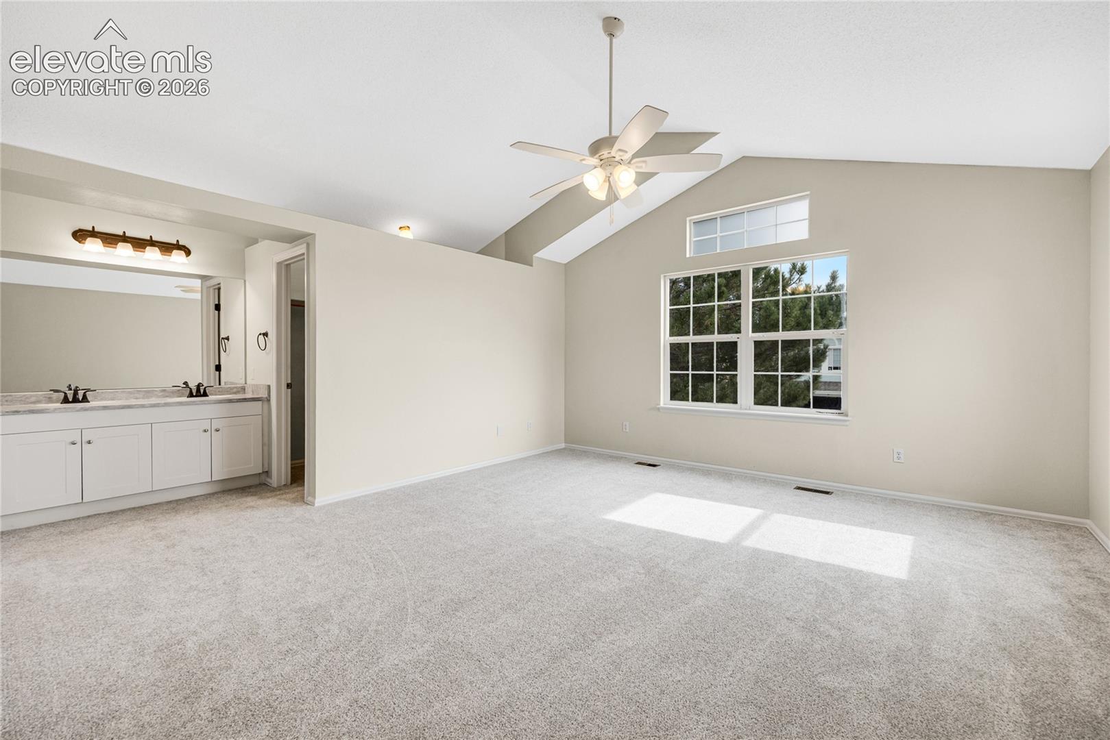 Vaulted ceilings featuring a transom window, wall-to-wall carpeting, and an integrated vanity with a stone-surface countertop, dual-basin sink, and multi-bulb vanity light fixture