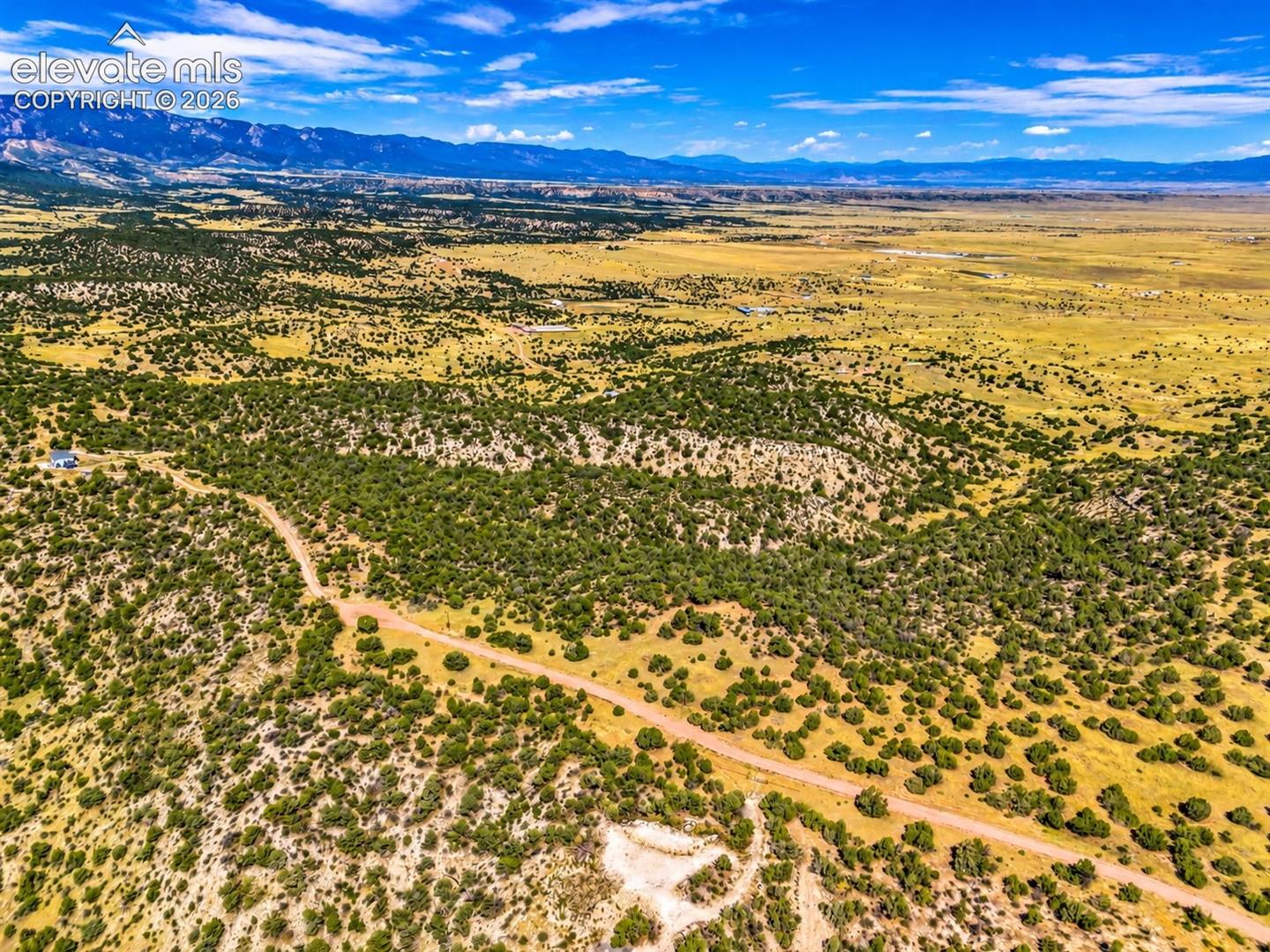 Sweeping aerial views of rugged mesas, natural ravines, and juniper-covered hillsides overlooking expansive high-desert valleys.

