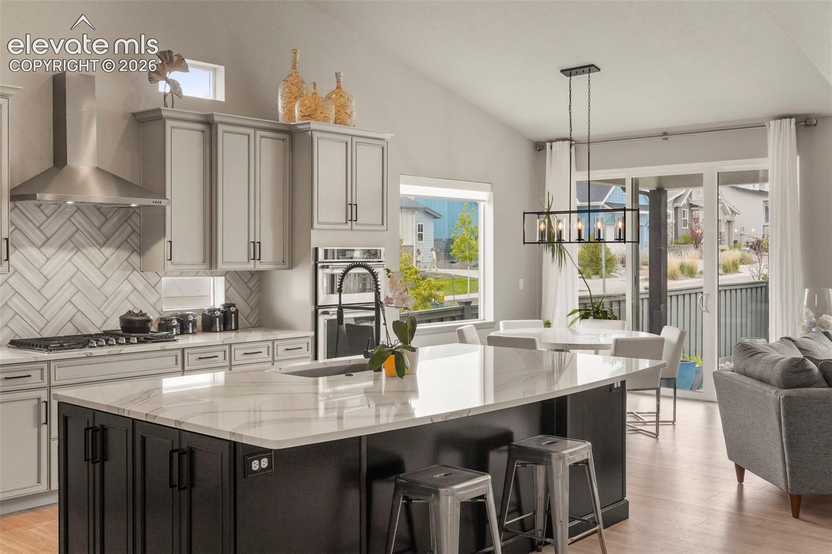 Modern kitchen featuring a large island with a light-toned countertop, contrasting dark cabinetry, stainless steel appliances, a herringbone tile backsplash, and wood-finish flooring