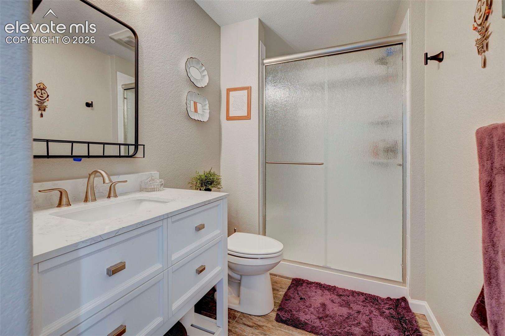 Bathroom featuring a white vanity with integrated basin, light-toned stone-finish countertop, brushed metal hardware, framed mirror, and a walk-in shower with a sliding glass door
