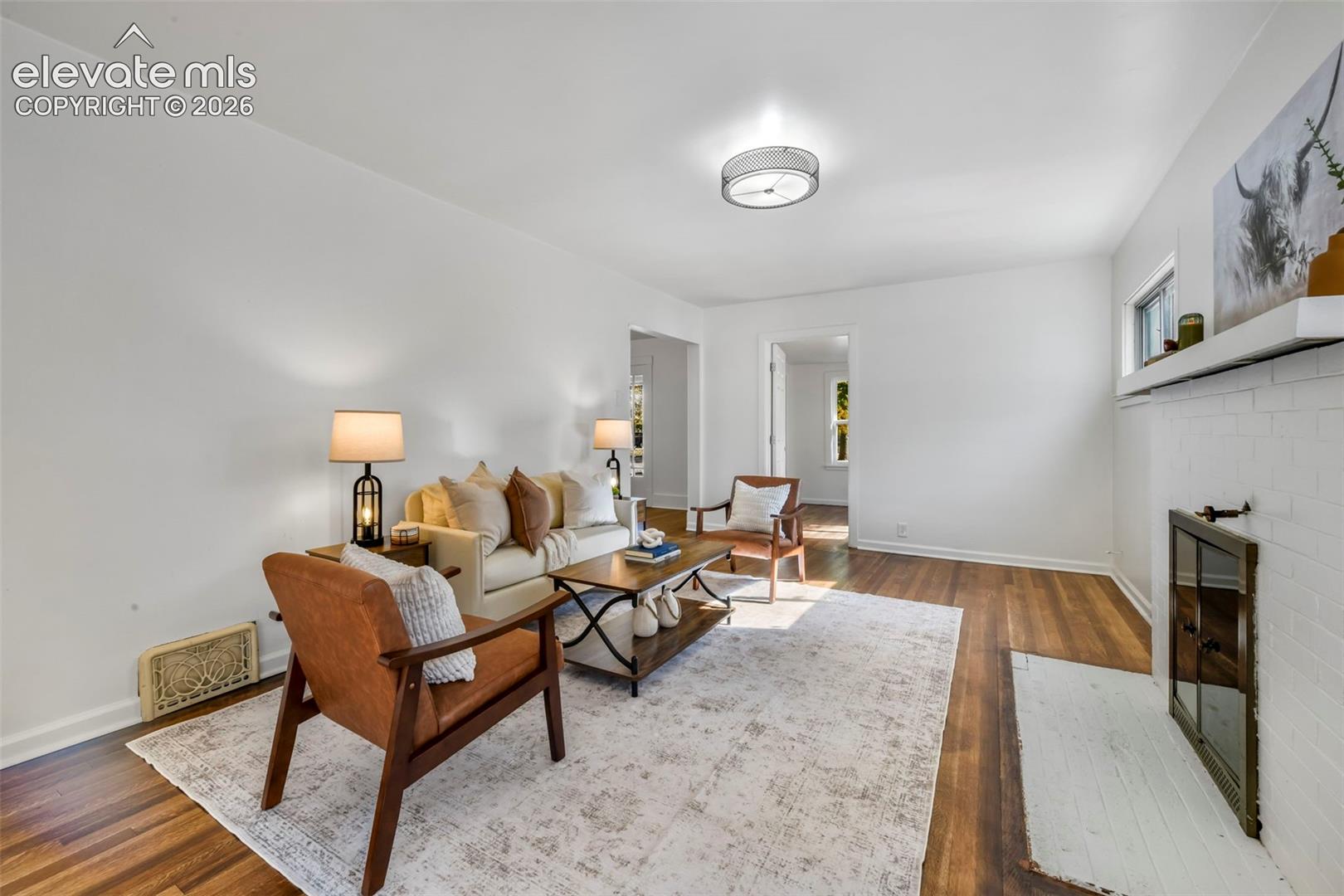 Living room featuring wood-finish flooring, white-painted brick fireplace with a mantle, and a circular flush-mount ceiling light fixture
