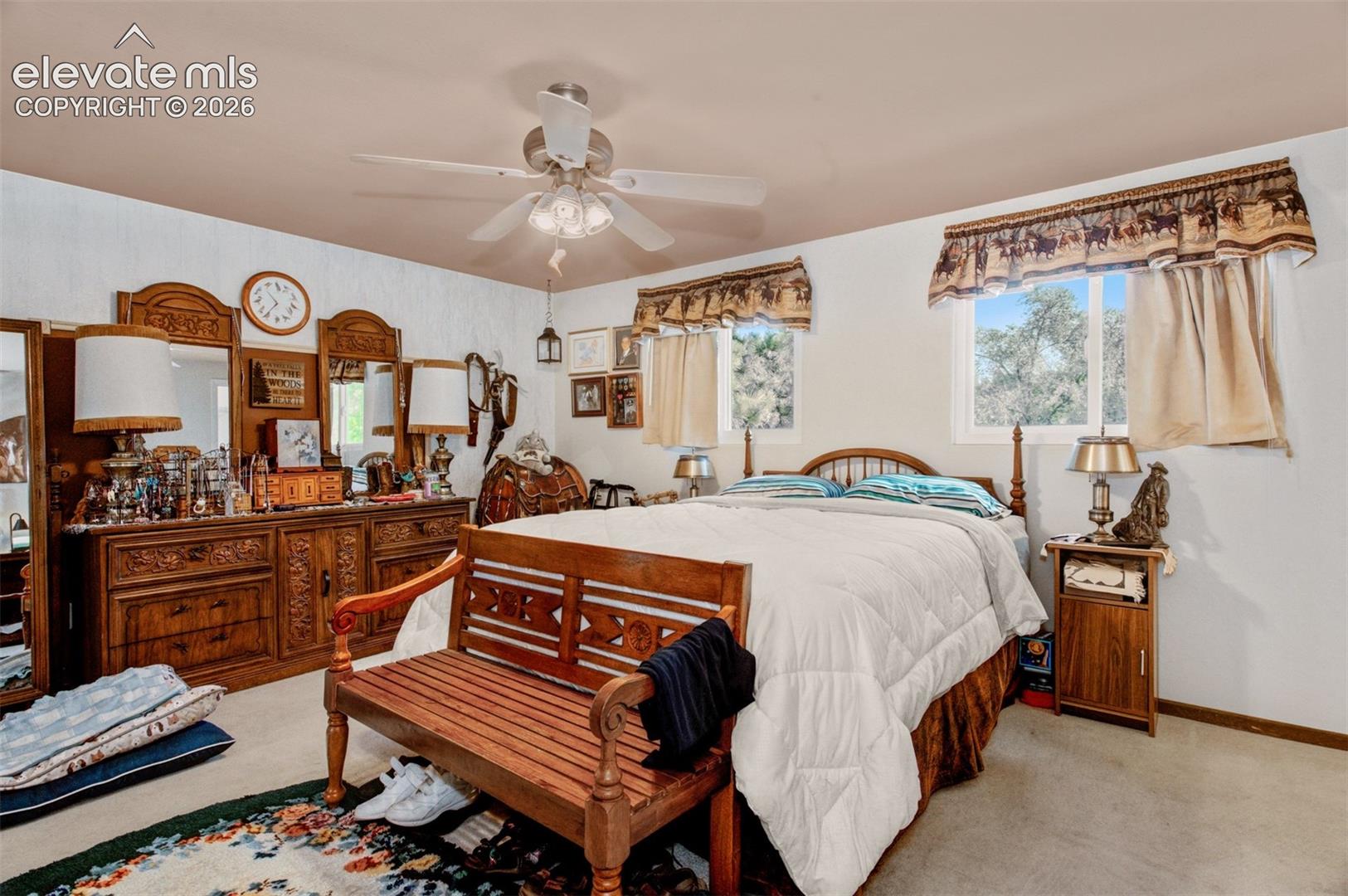 Spacious primary bedroom featuring rich wood furnishings, ceiling fan with integrated lighting, wood-finish flooring, and abundant natural light from multiple windows with fabric window treatments