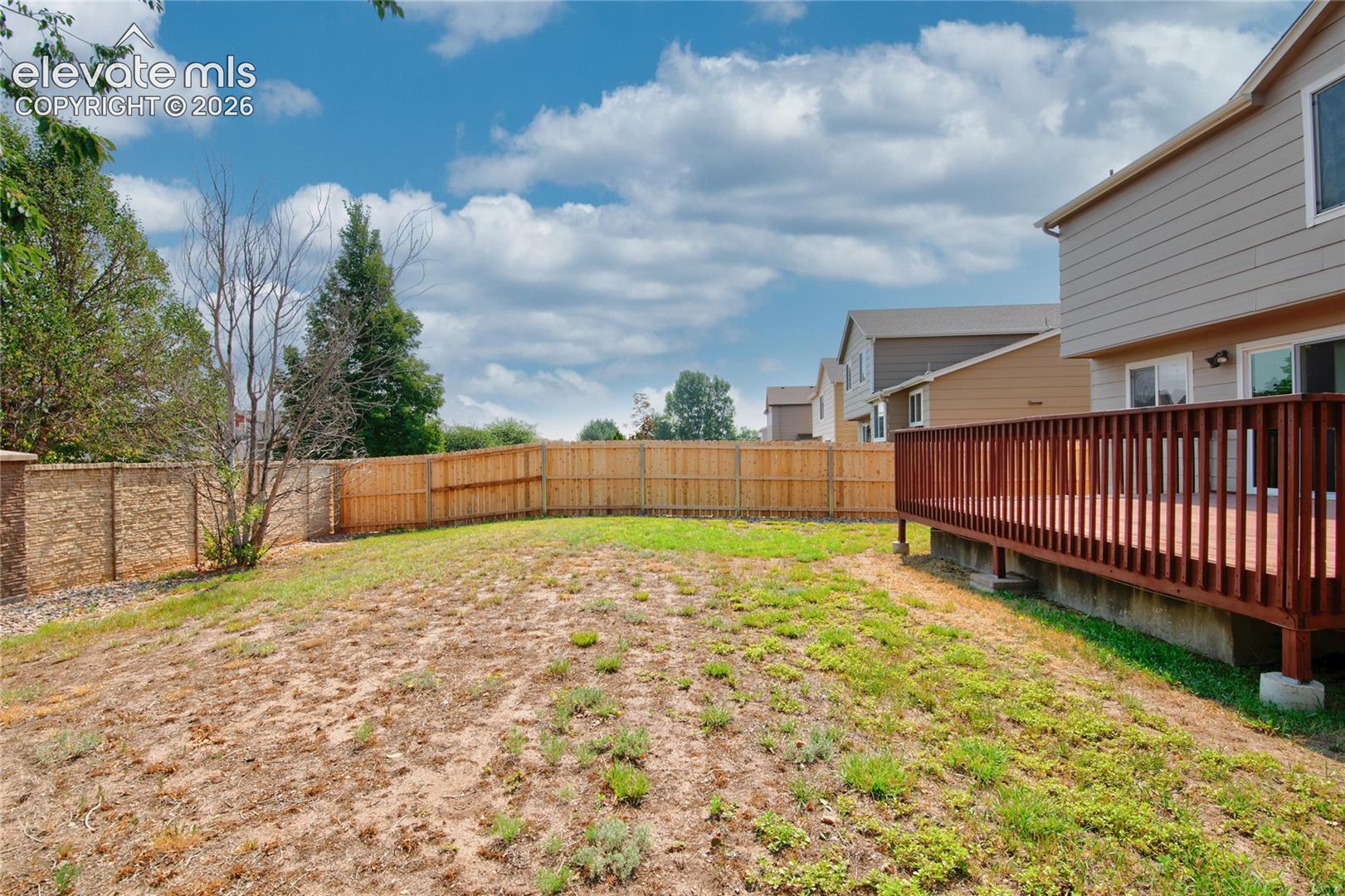 Expansive outdoor area featuring a wooden privacy fence, a retaining wall, and an elevated wood-tone deck