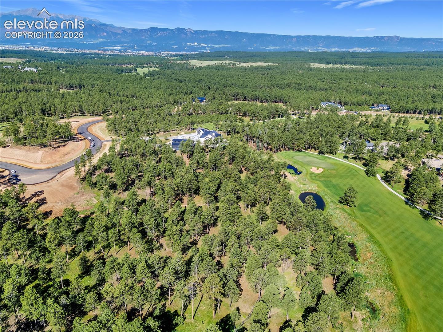 Aerial perspective featuring an expansive forested lot, direct proximity to a golf course fairway, multiple ponds, and prominent mountain backdrops
