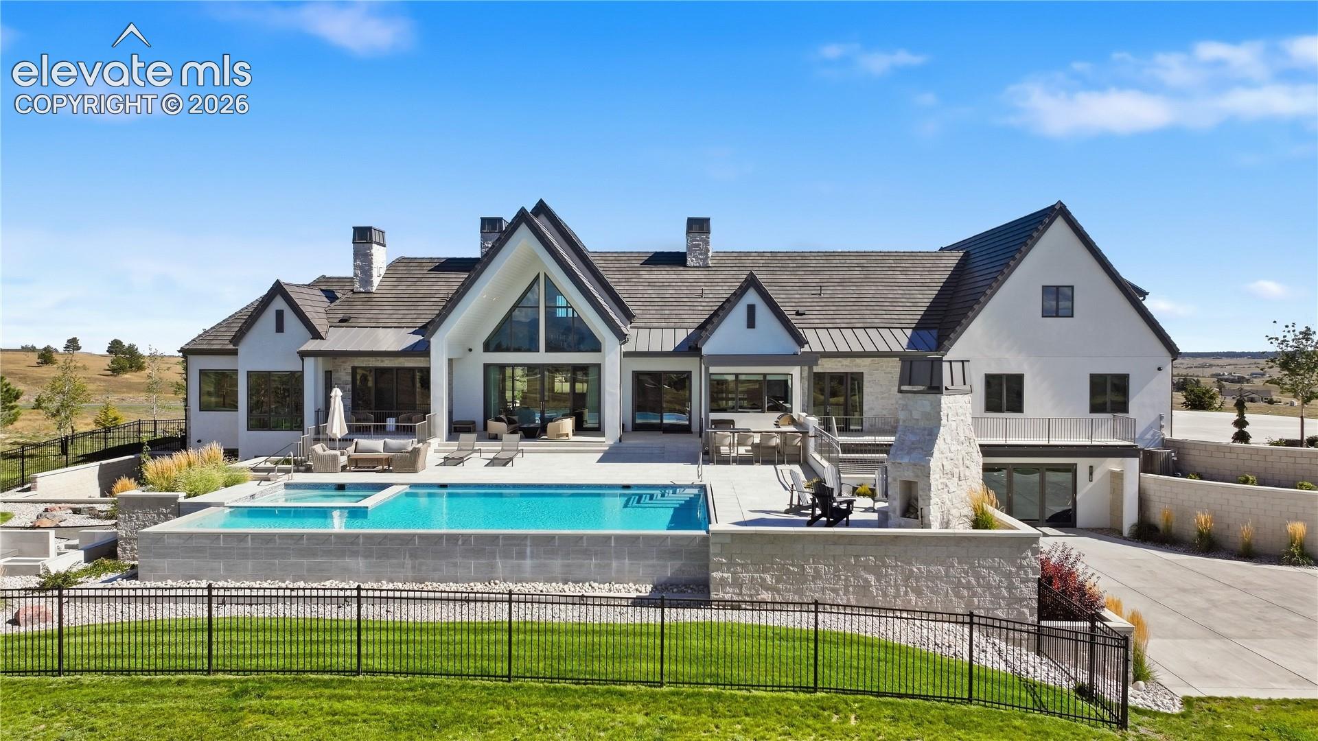 Multi-gabled exterior featuring white masonry and stone siding, expansive rear stone patio, elevated infinity-edge pool, and built-in outdoor stone fireplace