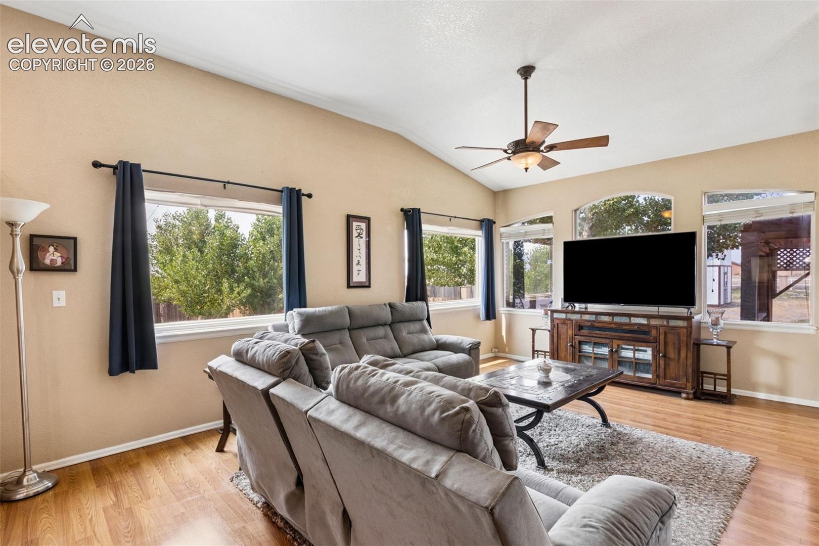 Vaulted ceilings, wood-finish flooring, multi-pane windows, and a ceiling fan with integrated lighting