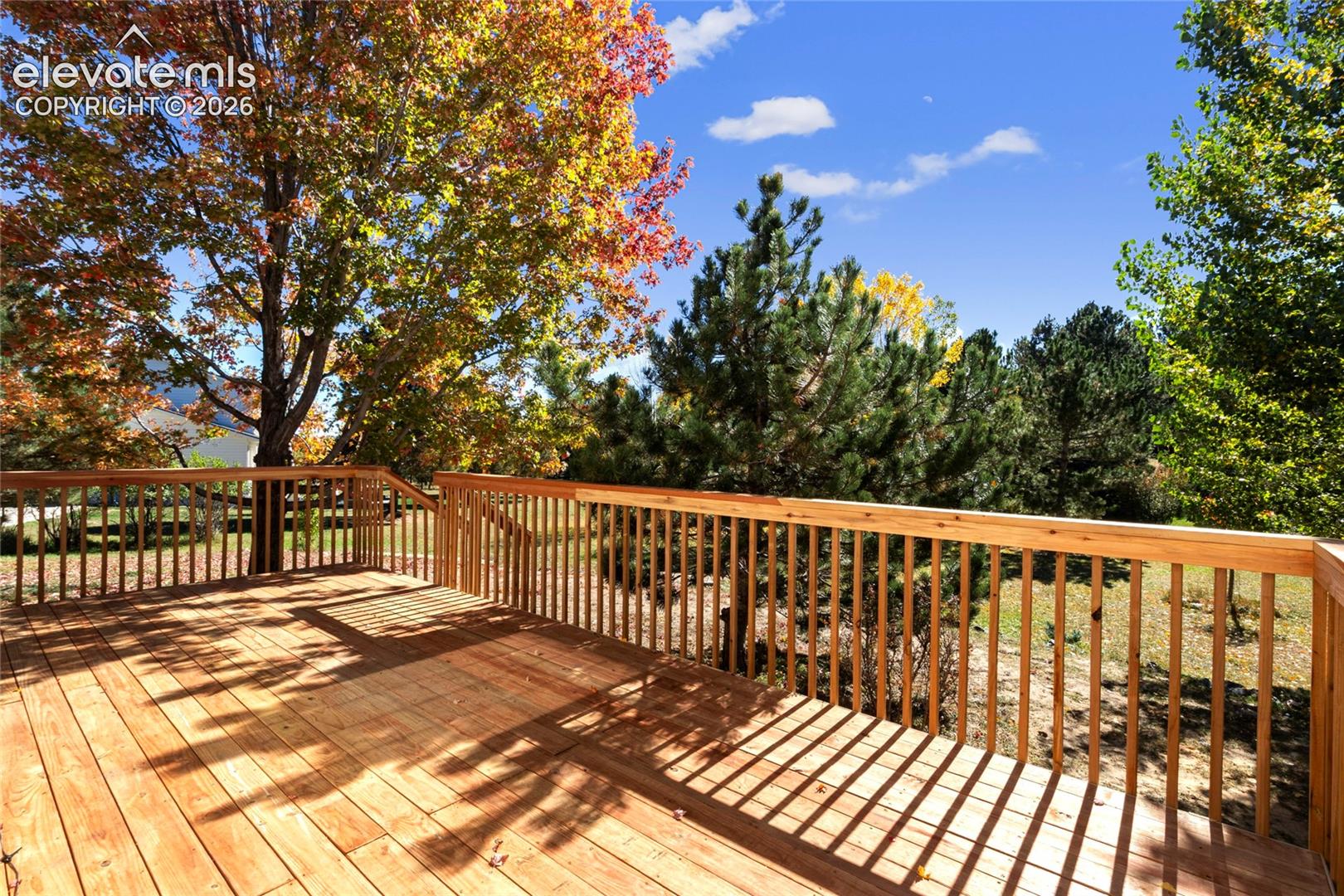Elevated wooden deck featuring vertical baluster railings and expansive natural surroundings with mature trees
