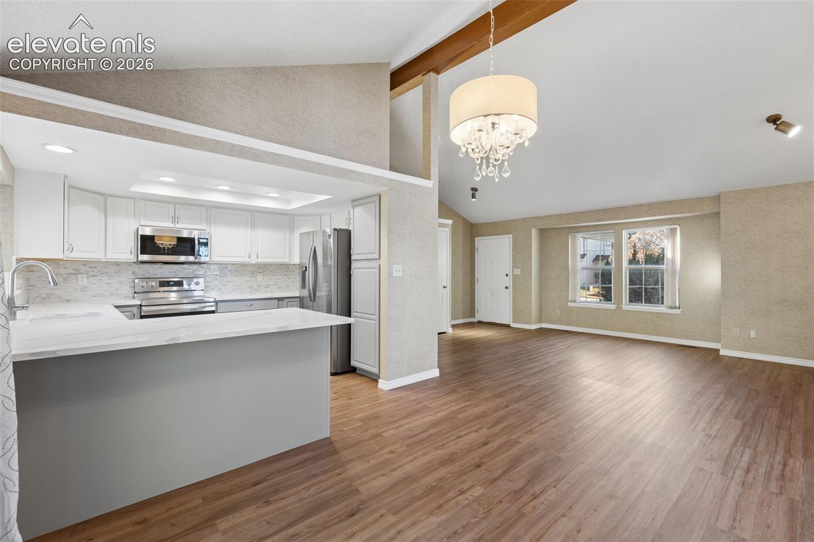 Kitchen featuring white cabinetry, wood-finish flooring, a quartz countertop, and vaulted ceilings with exposed wood beams