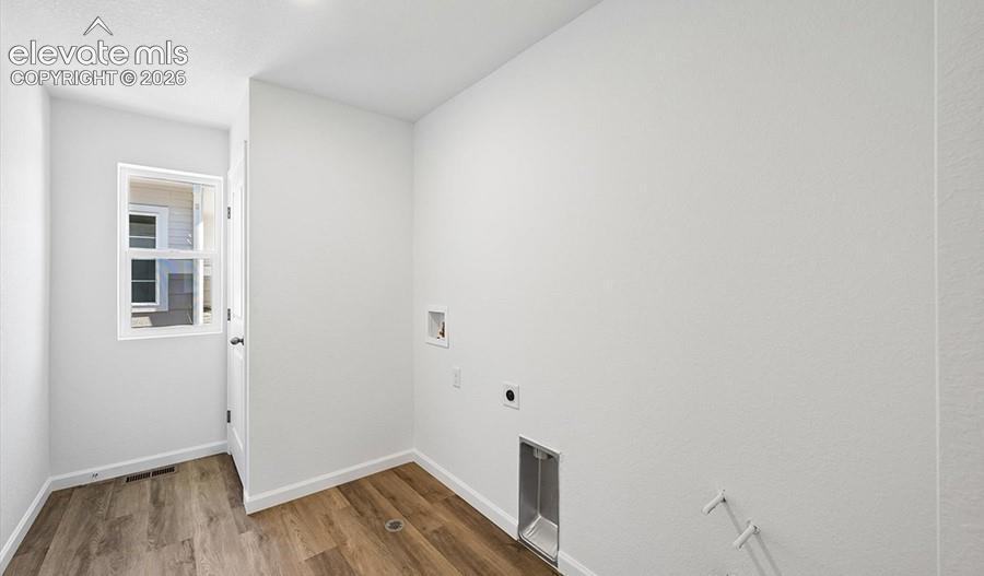 Utility area featuring wood-finish flooring, white walls, a single-pane window, and built-in water and electrical hookups