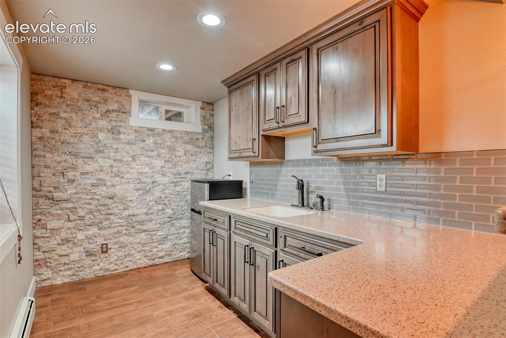 Kitchen with light stone counters, light wood-type flooring, a baseboard radiator, tasteful backsplash, and recessed lighting