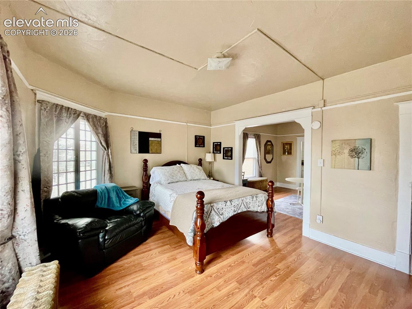 Spacious primary bedroom with wood-finish flooring, decorative ceiling detail, and abundant natural light from multi-pane windows