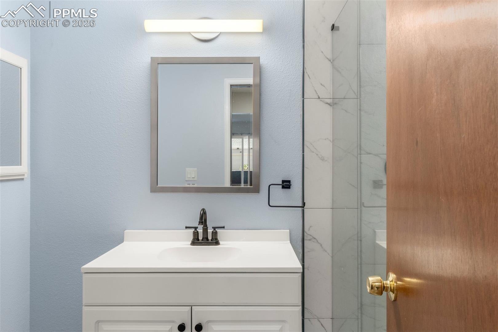 Full bathroom featuring vanity, a marble finish shower, and a textured wall