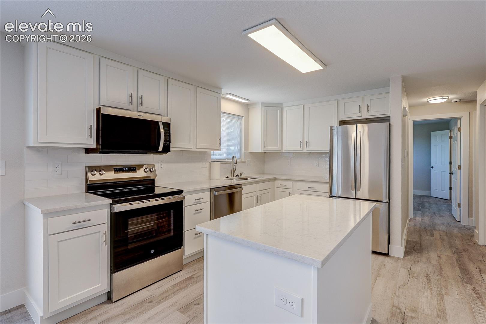 Kitchen featuring white cabinetry, solid-surface countertops, center island, stainless steel appliances, and wood-finish flooring