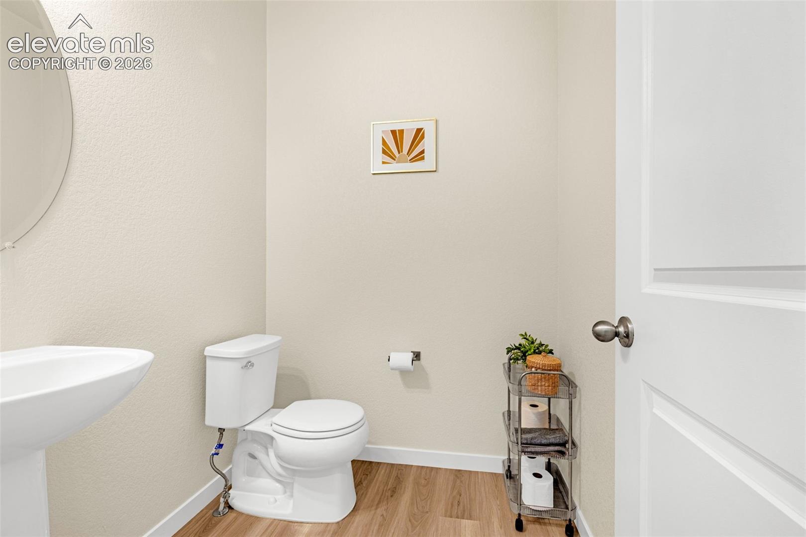 Pedestal sink with an oval mirror, light-colored walls, wood-finish flooring, and a white interior door