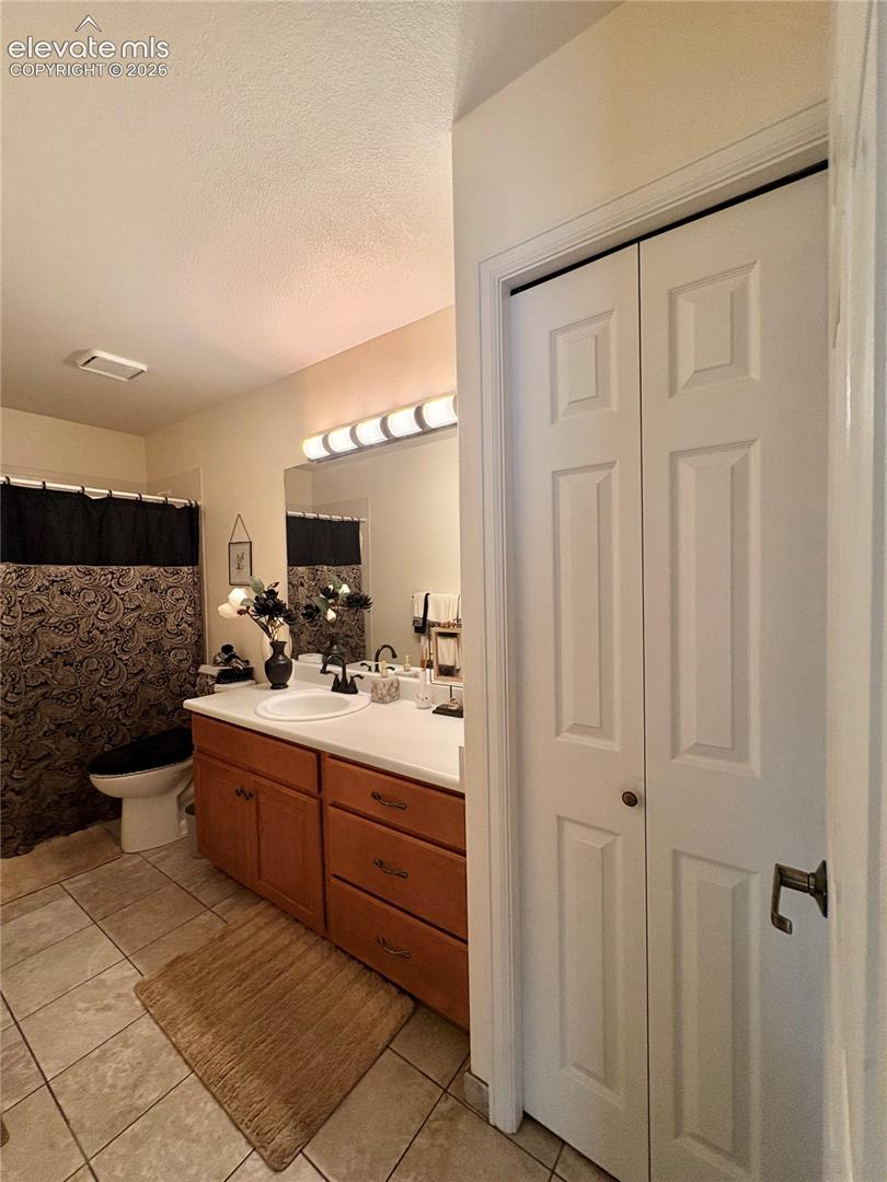 White panel bi-fold doors, tile flooring, wood-finish vanity with built-in storage, white countertop, and integrated sink