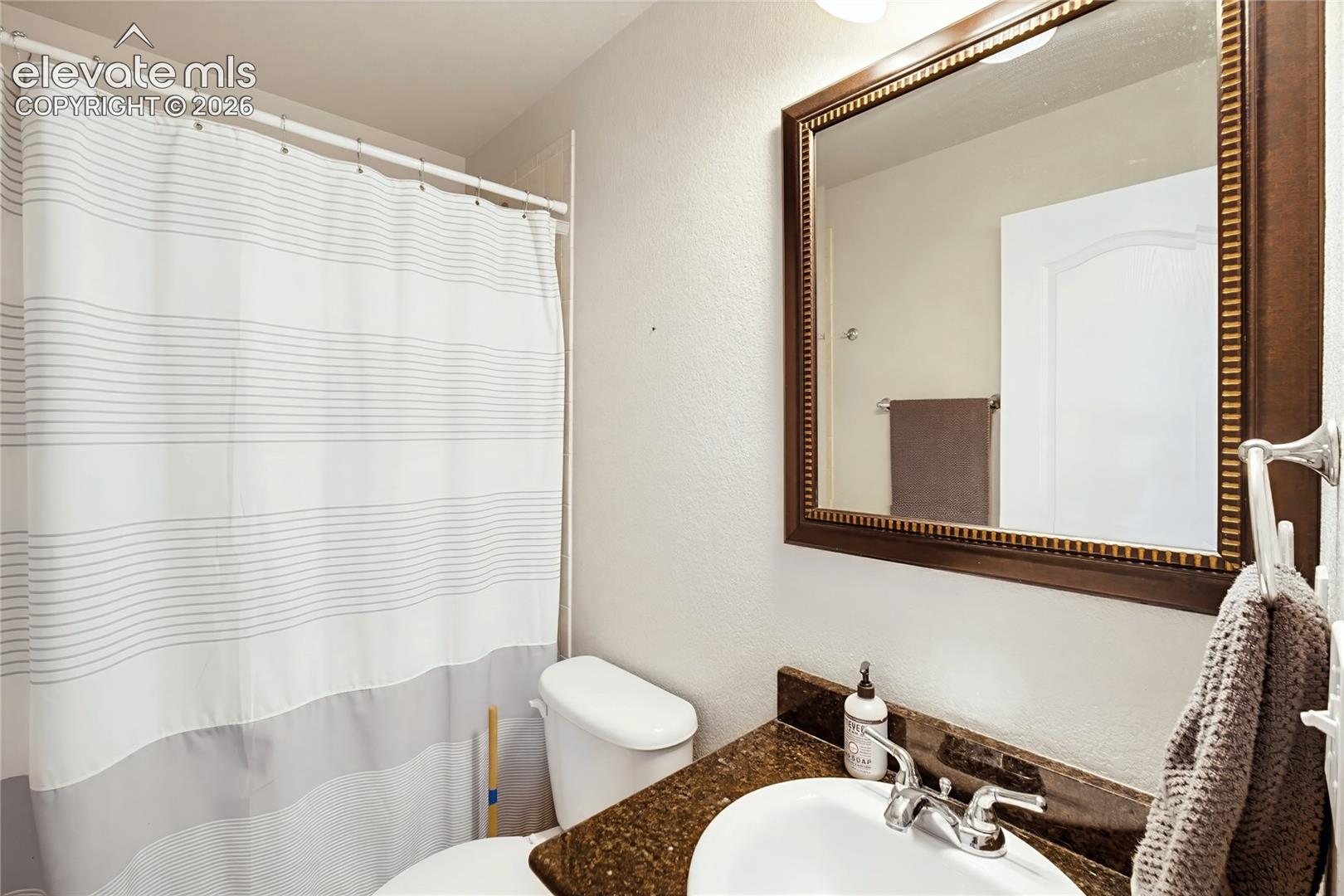 Bathroom featuring a dark stone-finish countertop, white oval undermount sink, chrome double-handle faucet, and framed wall mirror