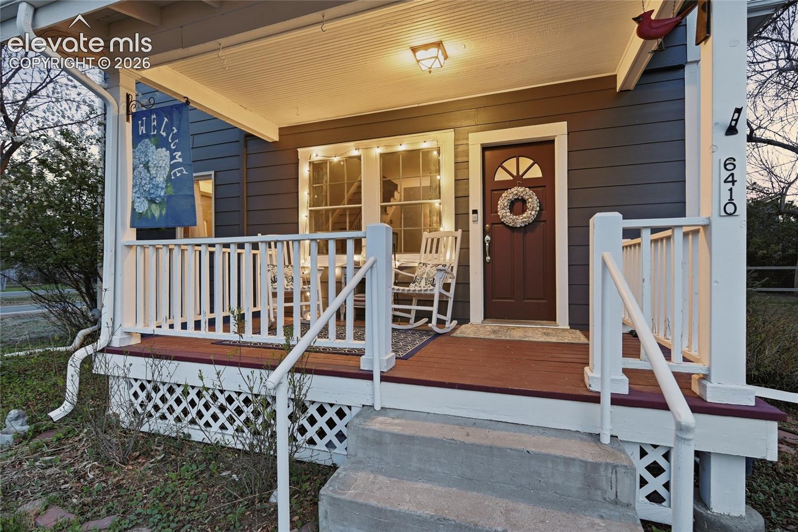Covered front porch with white railing, wood-tone decking, lattice skirting, and horizontal lap siding