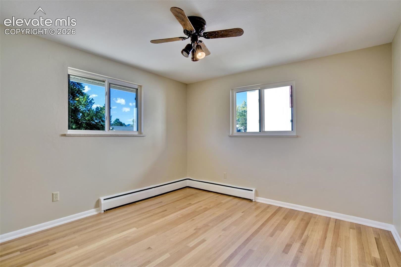 Neutral wall tones, wood-finish flooring, dual sliding windows, and a ceiling-mounted light fixture with a fan