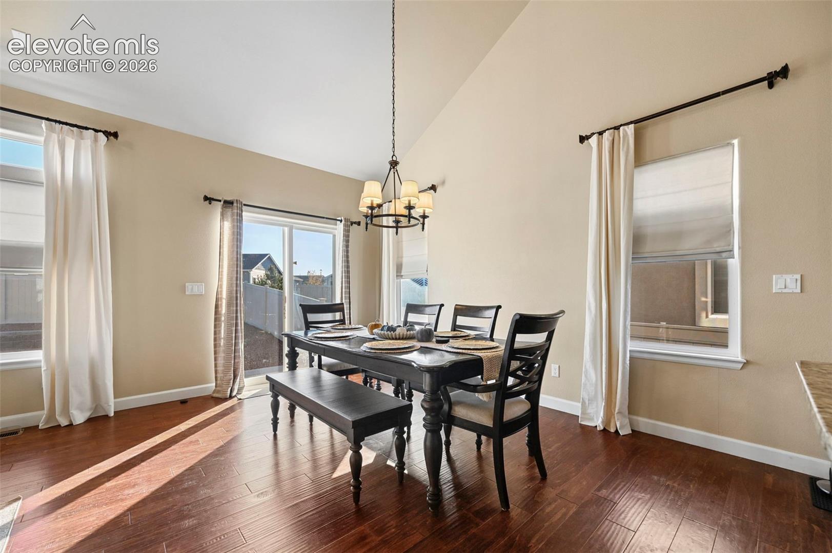 Vaulted ceiling featuring a chandelier, wood-finish flooring, sliding glass door, and multiple windows