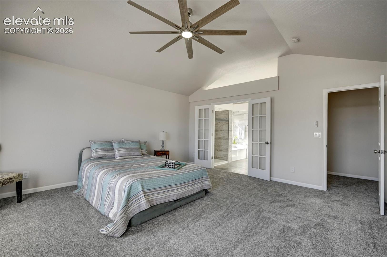 Vaulted ceiling with an integrated multi-blade ceiling fan, neutral wall tones, plush wall-to-wall carpeting, and double French doors with glass panes