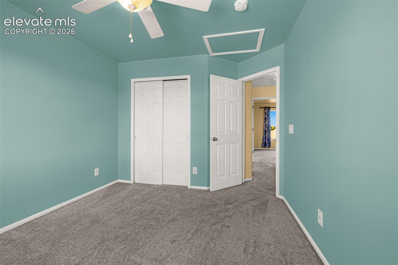Spacious bedroom featuring soft turquoise walls, neutral carpet flooring, a ceiling fan with integrated lighting, and dual closet doors providing ample storage