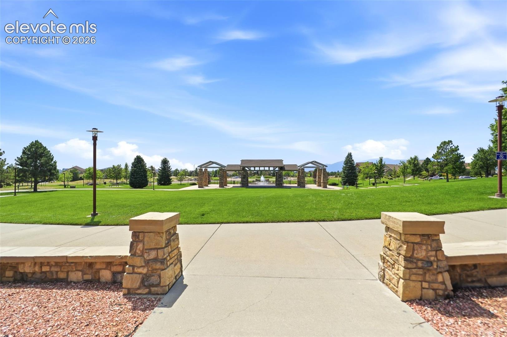 Expansive green space featuring a central fountain, stone-clad pergolas, and mature trees