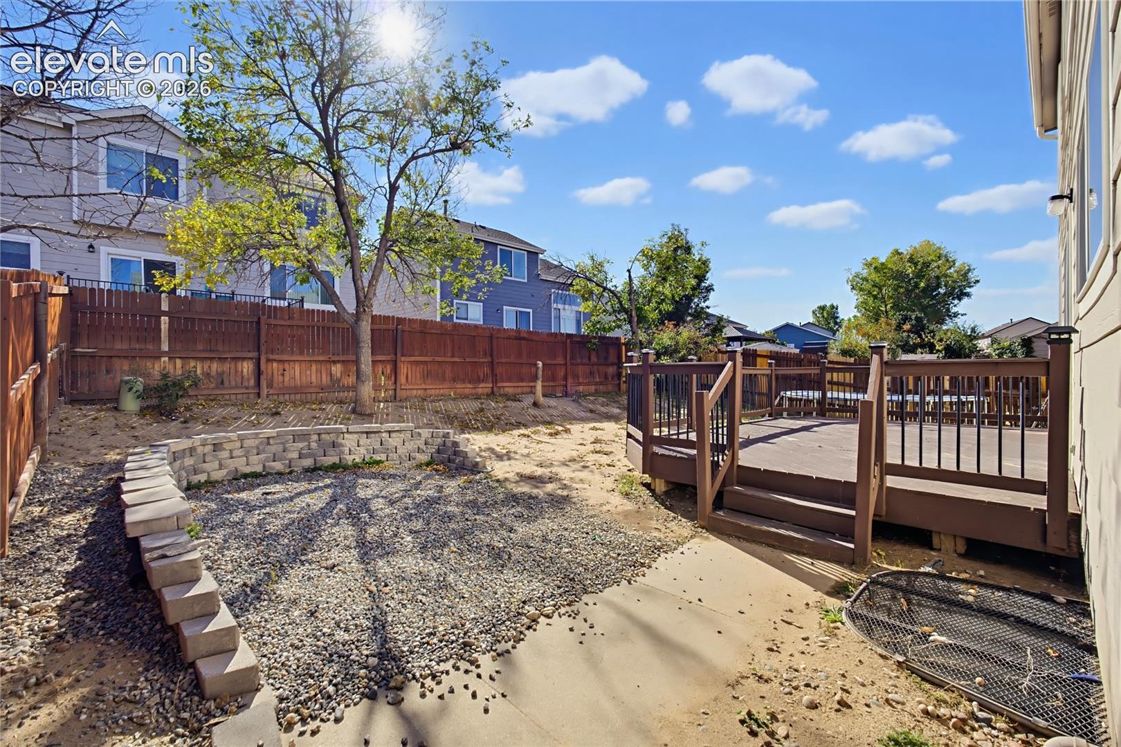 Outdoor space featuring a raised wooden deck with metal railing, stacked stone retaining wall, and wood privacy fencing