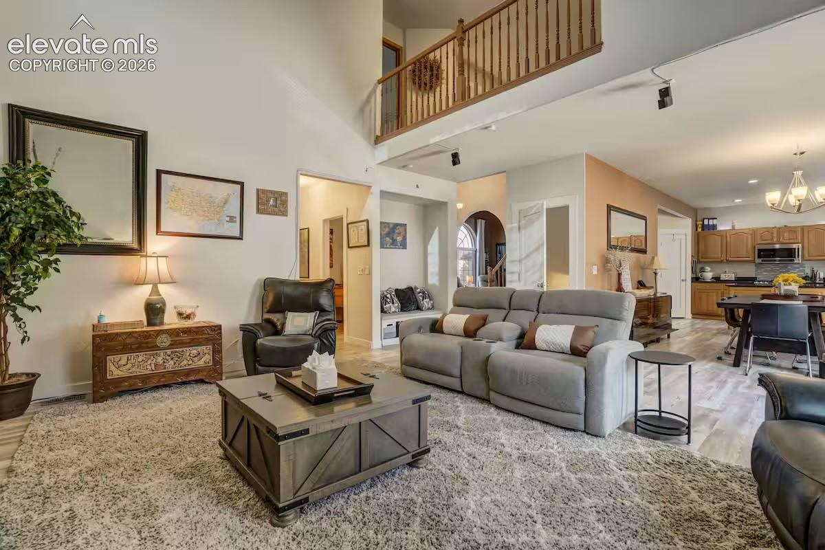 Spacious living area featuring high ceilings, a second-story balcony, light-toned wood-finish flooring, and an open concept to the kitchen and dining areas
