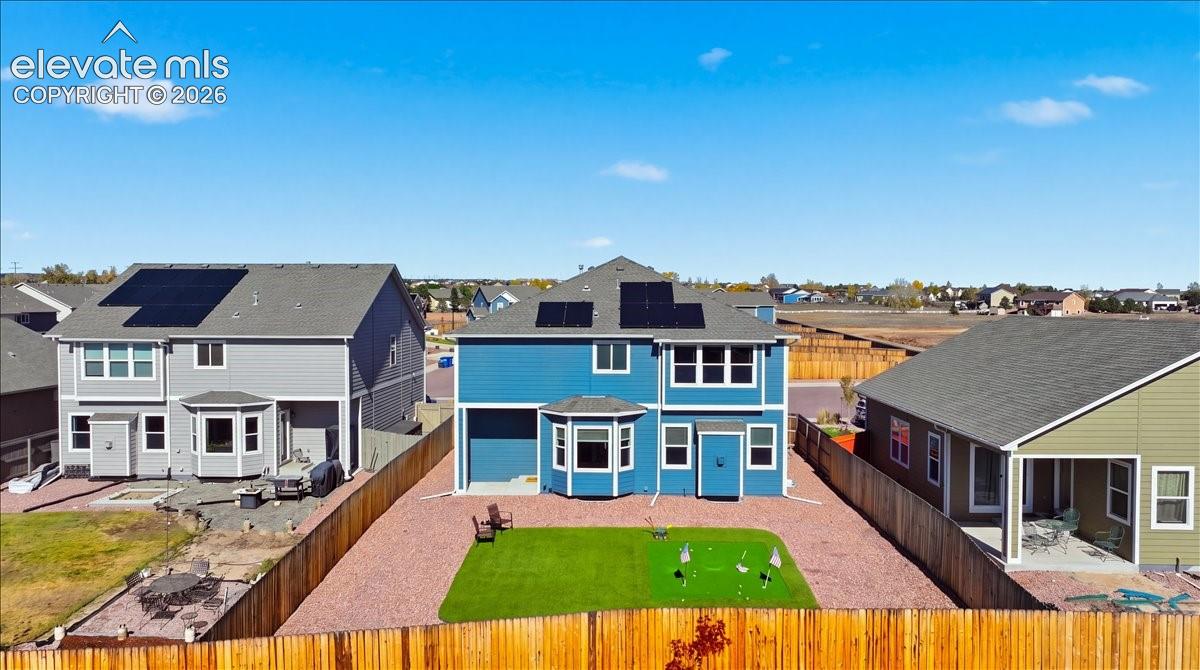 Exterior features include a blue-toned siding finish, solar panel arrays, a multi-paneled roof, a rear yard with a synthetic turf putting green, and perimeter wood fencing