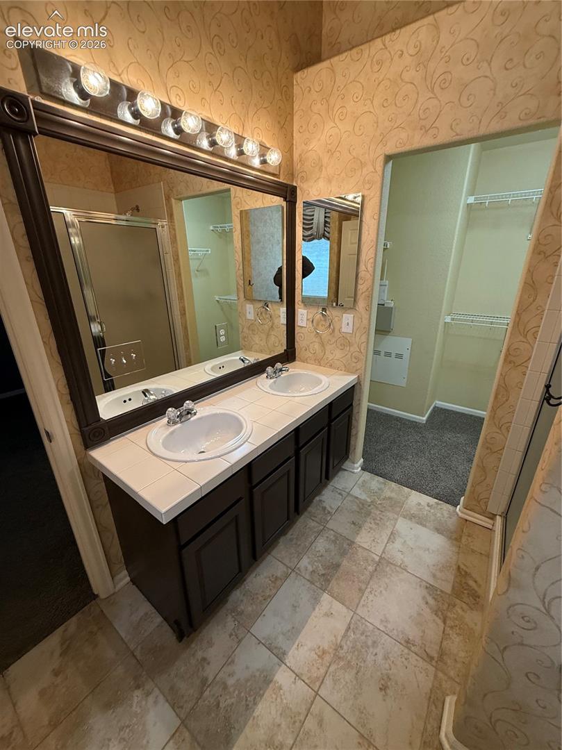 Double vanity featuring tile countertops, integrated dual sinks, dark-finish cabinetry, a full-width framed mirror, and tile flooring