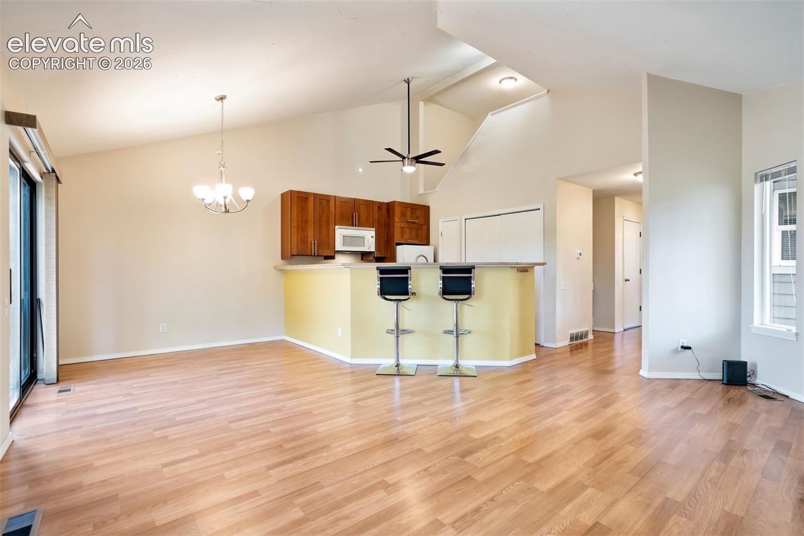 Vaulted ceilings, wood-finish flooring, peninsula kitchen cabinetry, multi-light chandelier, and sliding glass door