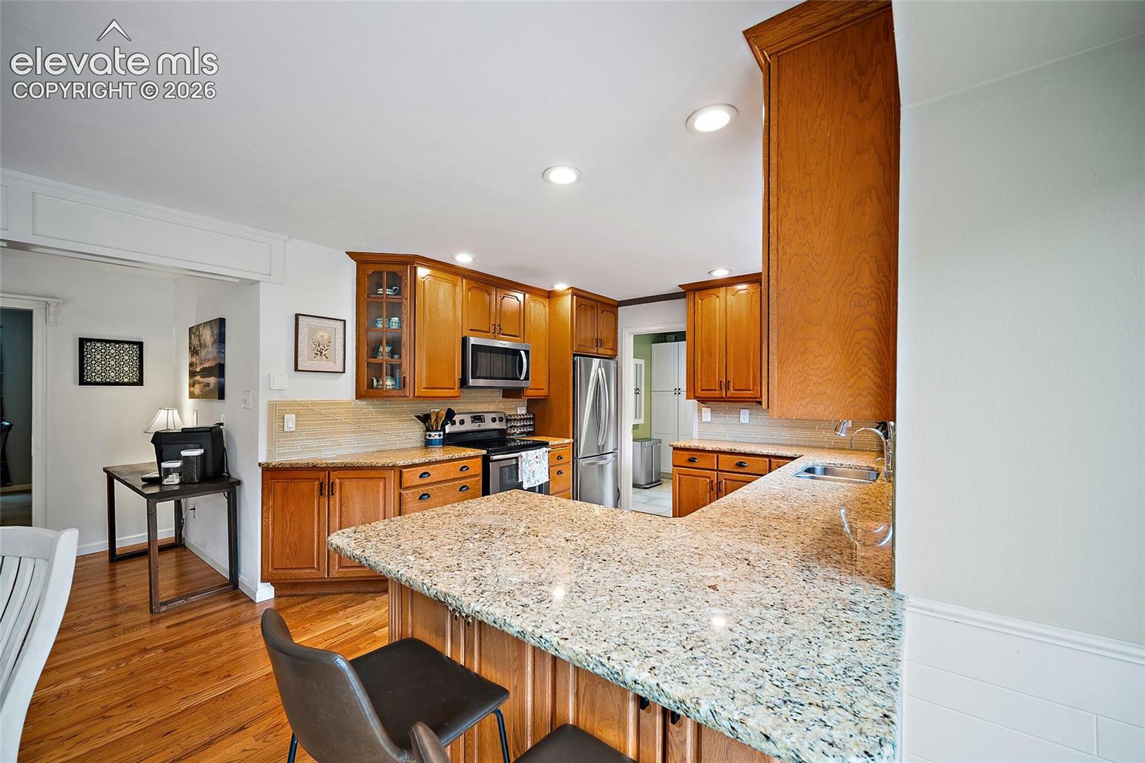 Kitchen featuring stone countertops, wood-finish cabinetry, stainless steel appliances, recessed lighting, and wood-finish flooring