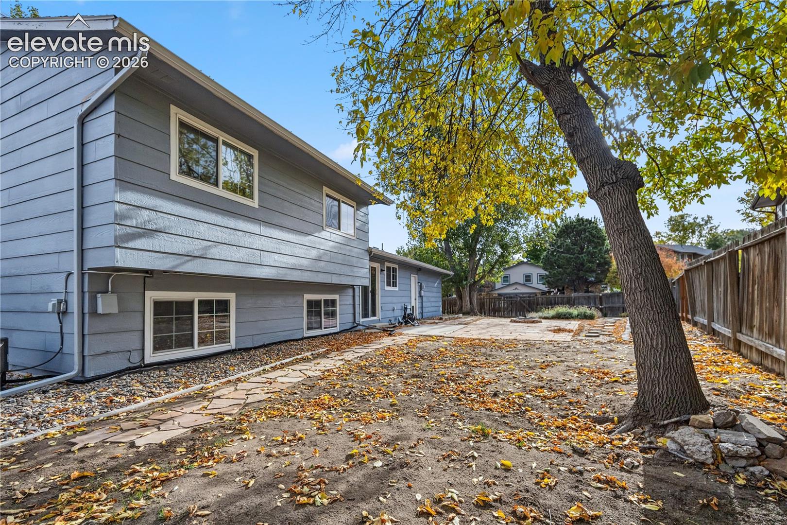 Horizontal siding exterior featuring a paved stone patio, flagstone pathway, and perimeter wood fencing
