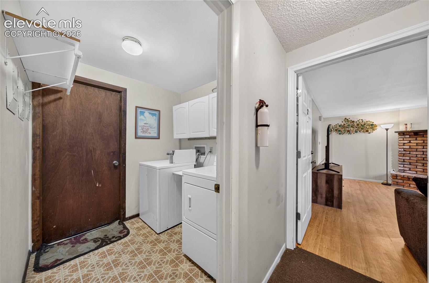 Laundry room featuring overhead cabinetry, patterned sheet flooring, a dedicated wash-basin hookup, and a wood-finish door