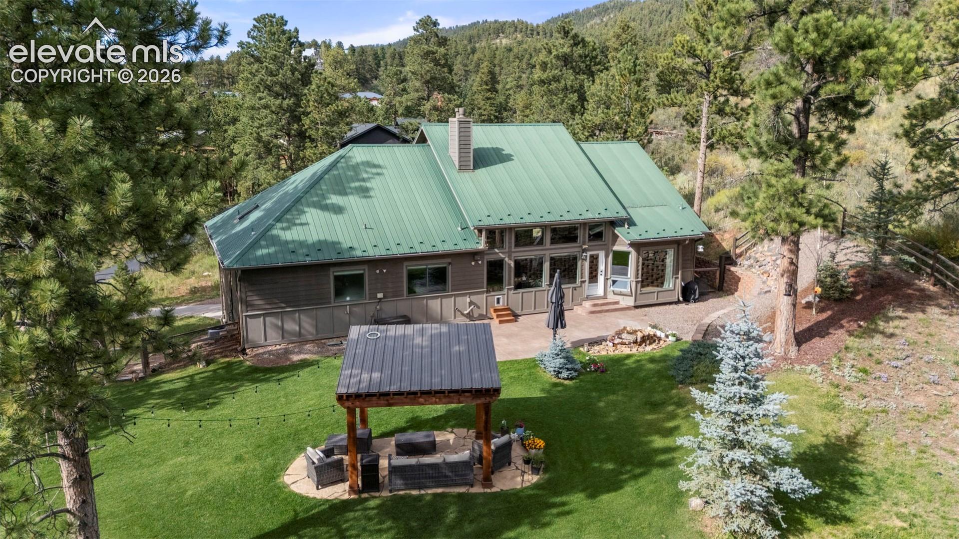 Back of property featuring a patio area, a metal roof, a wooded view, outdoor lounge area, and a lawn