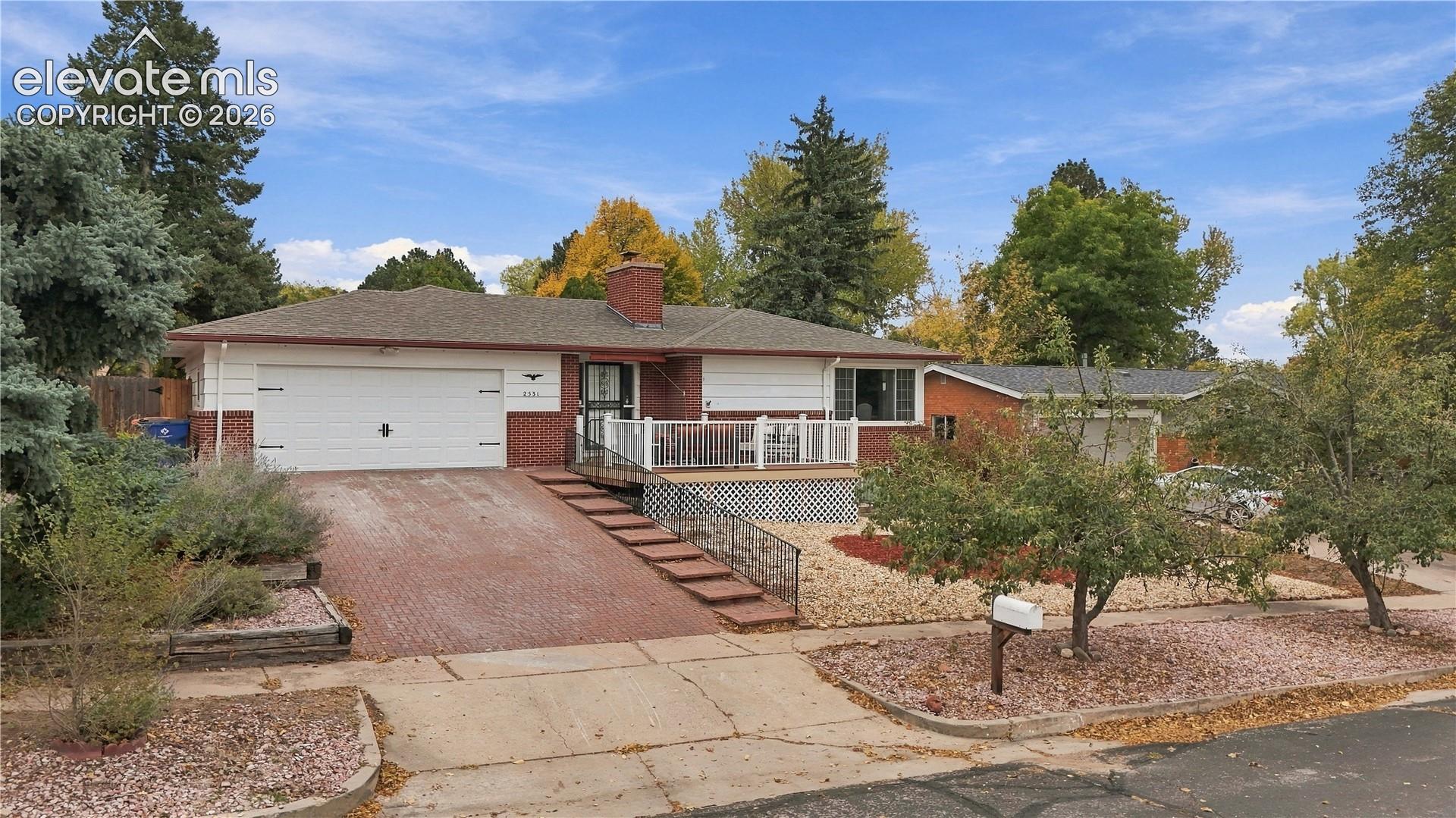 Single-story residence featuring a brick and horizontal siding exterior, attached two-car garage, elevated front deck, and masonry chimney
