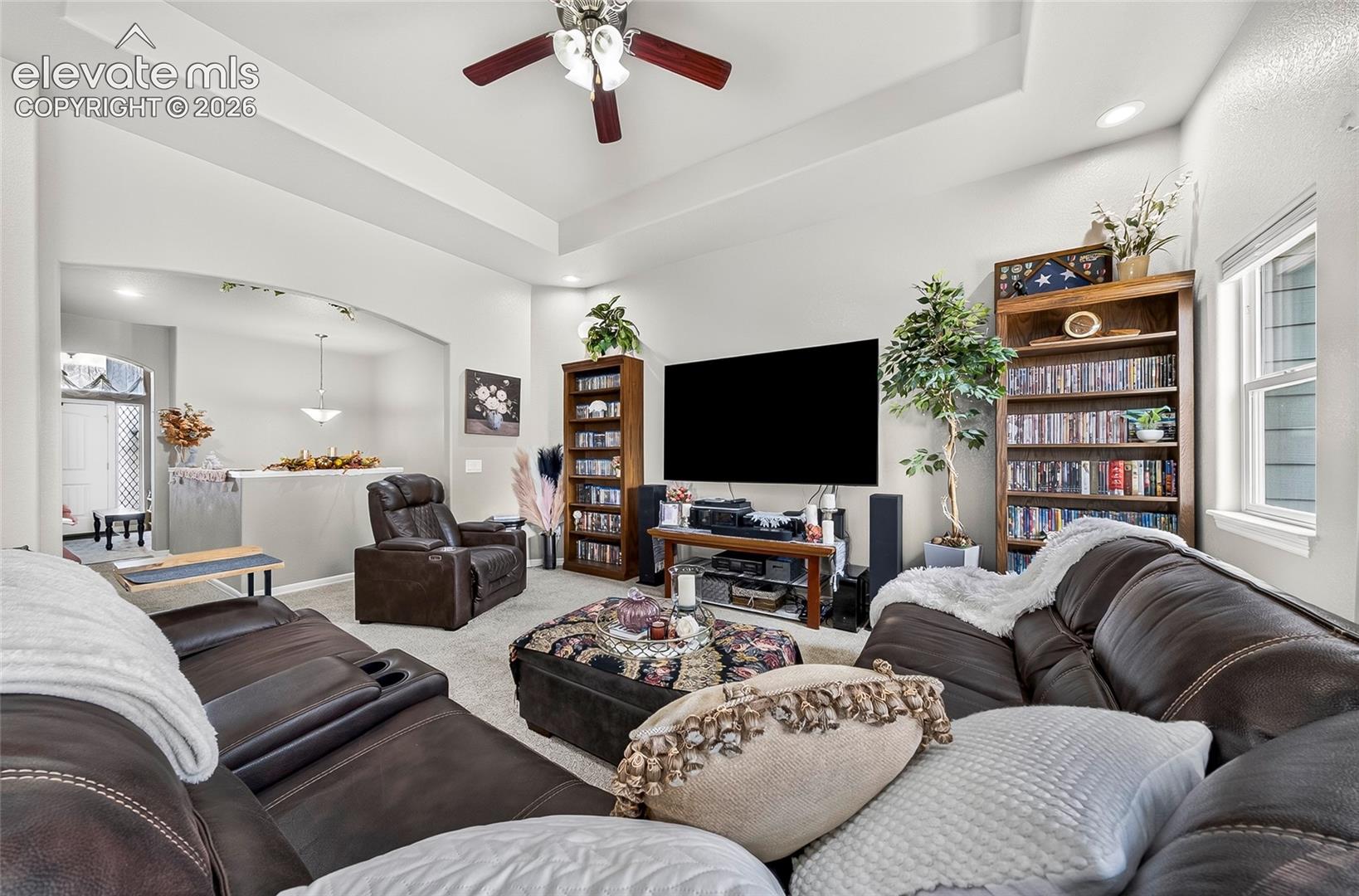 Living area featuring a tray ceiling, recessed lighting, ceiling fan, and arched entryway