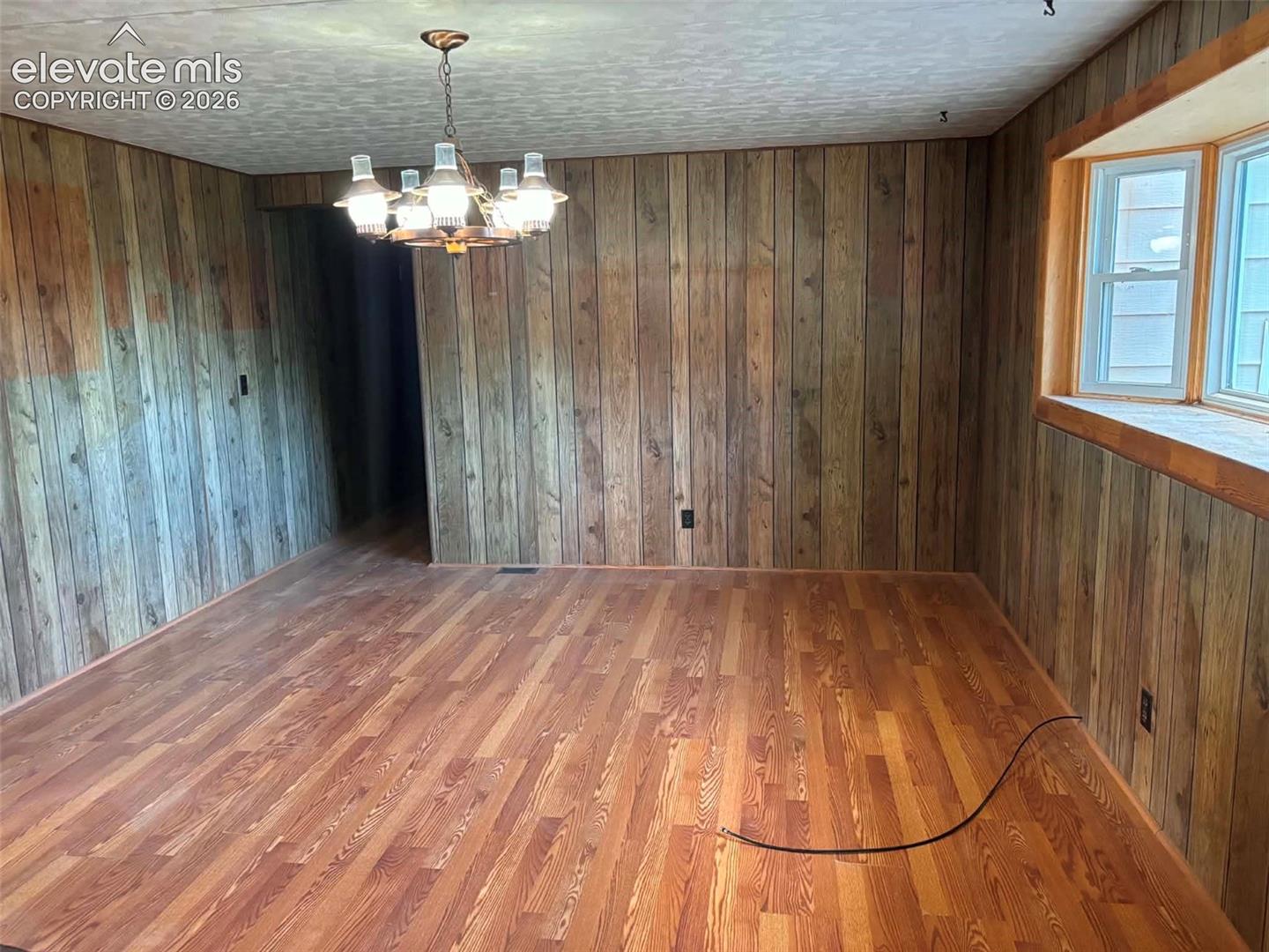 Room featuring wood-paneled walls, wood-finish flooring, a bay window, and a multi-arm chandelier