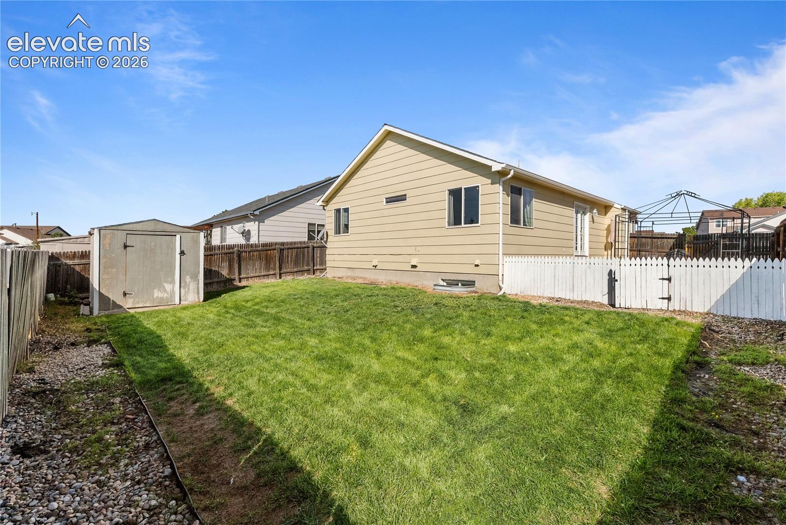 Expansive backyard featuring a manicured lawn, white picket fence, and a storage shed
