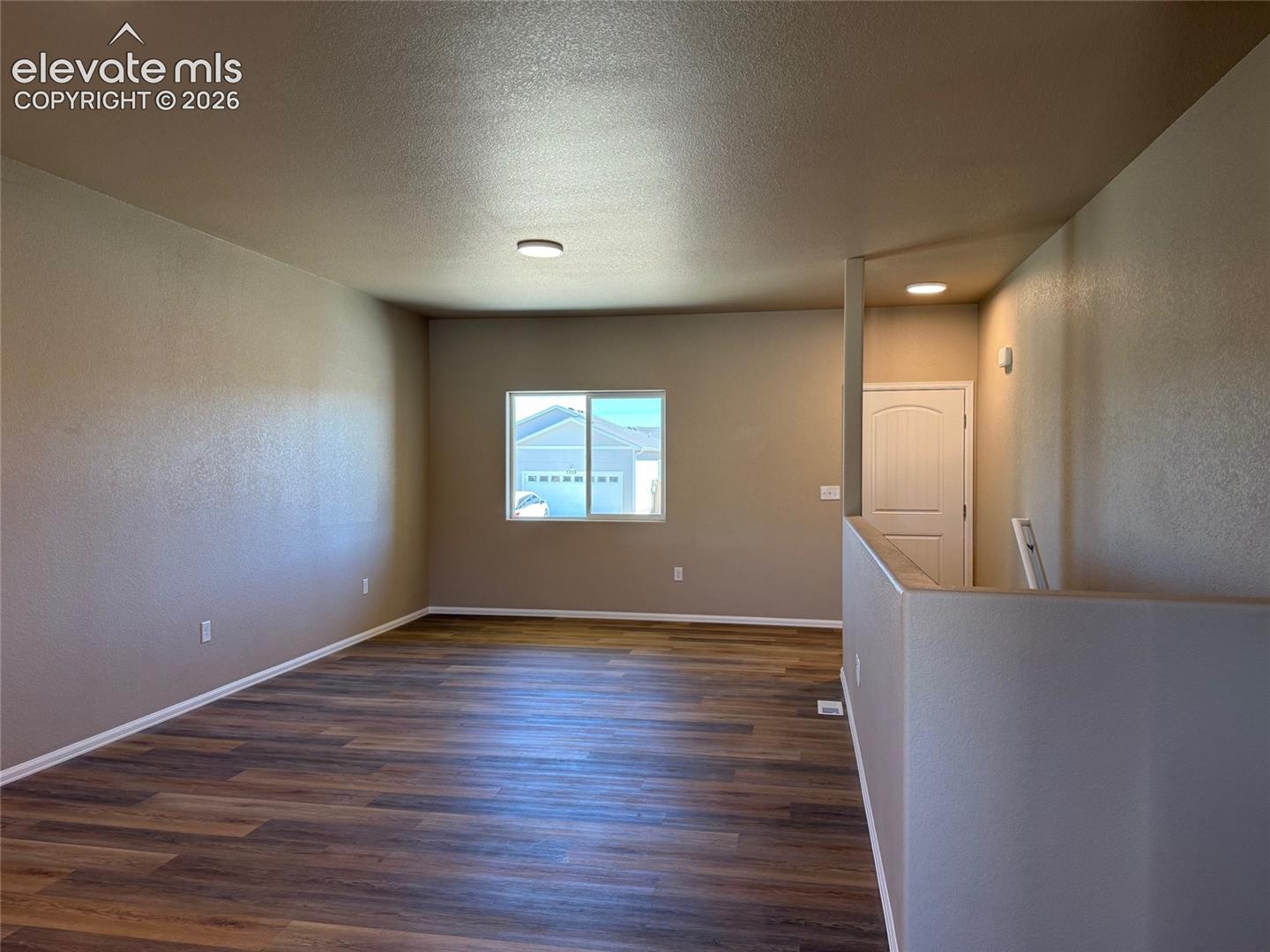 Wood-finish flooring, neutral wall tones, window with white trim, white paneled door, and flush-mount lighting