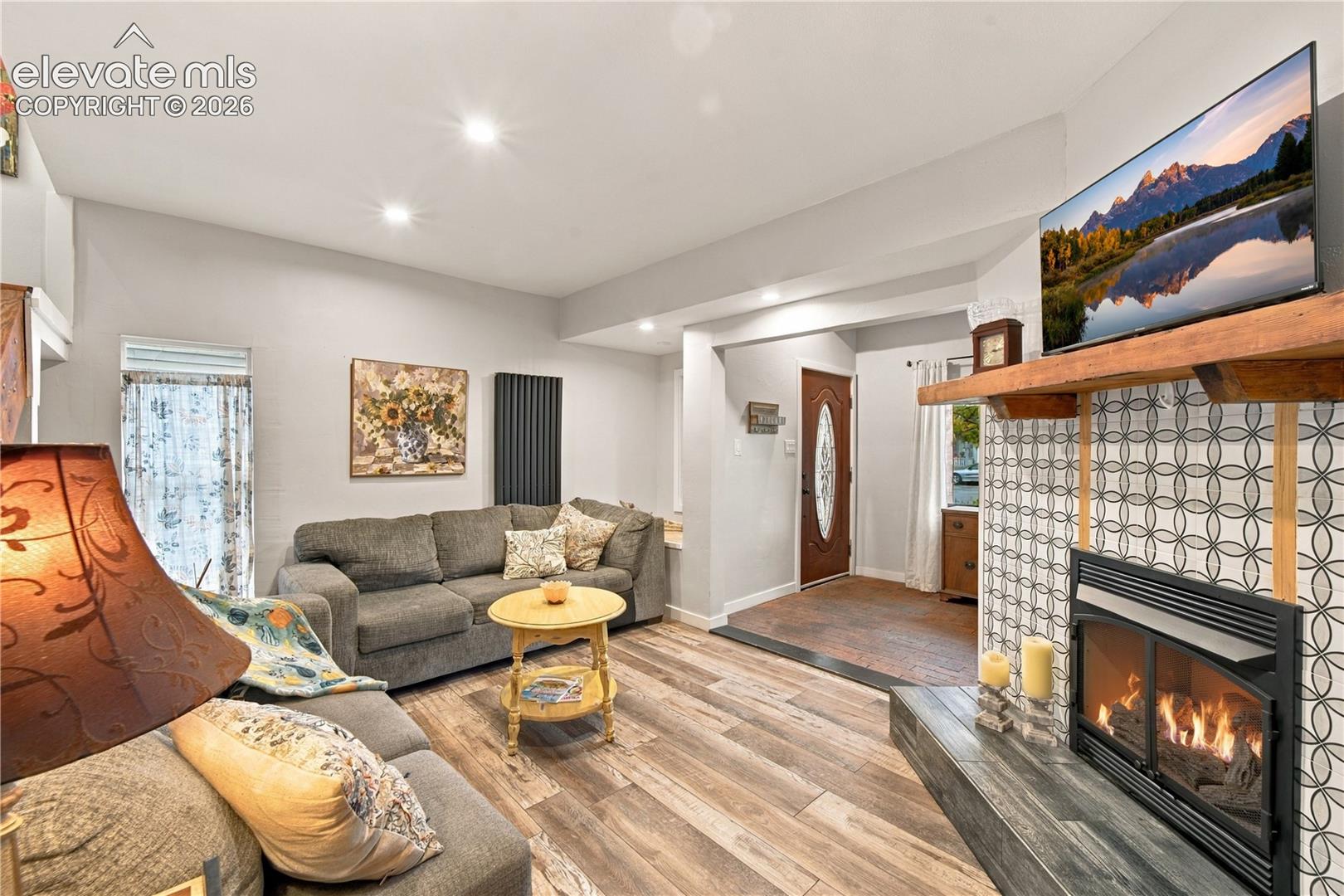 Living area featuring wood-finish flooring, recessed lighting, and a fireplace with decorative tile surround and natural wood mantel
