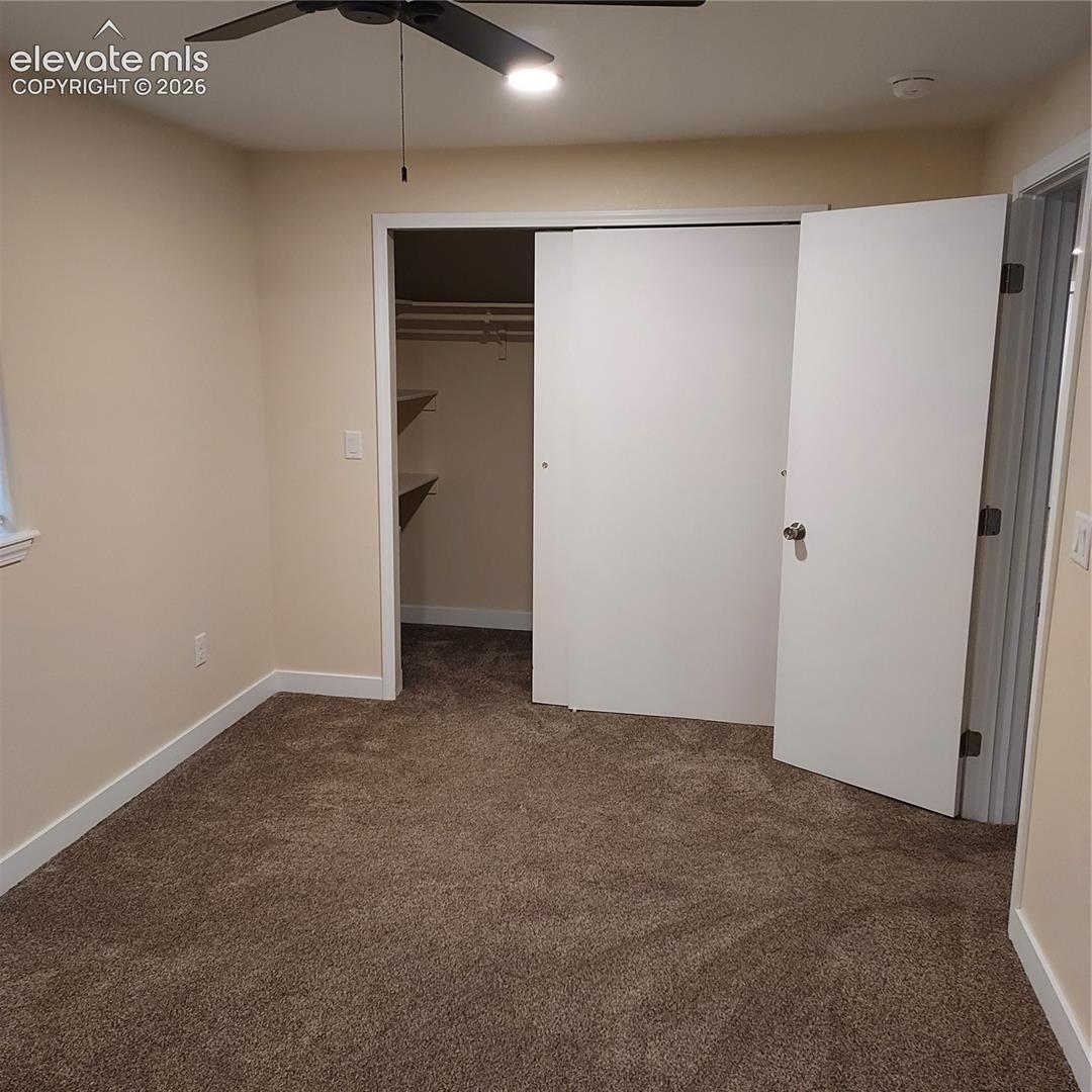 Room interior featuring plush wall-to-wall carpeting, a sliding door closet with built-in shelving, and a ceiling fan with integrated lighting