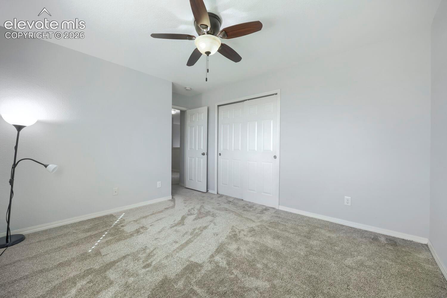 Neutral wall palette with plush carpeting, five-blade ceiling fan with central light fixture, and sliding closet doors