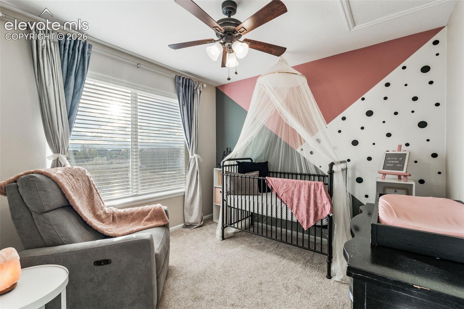 Bedroom featuring neutral carpeting, a central multi-blade ceiling fan with integrated lighting, and a multi-panel window with horizontal blinds