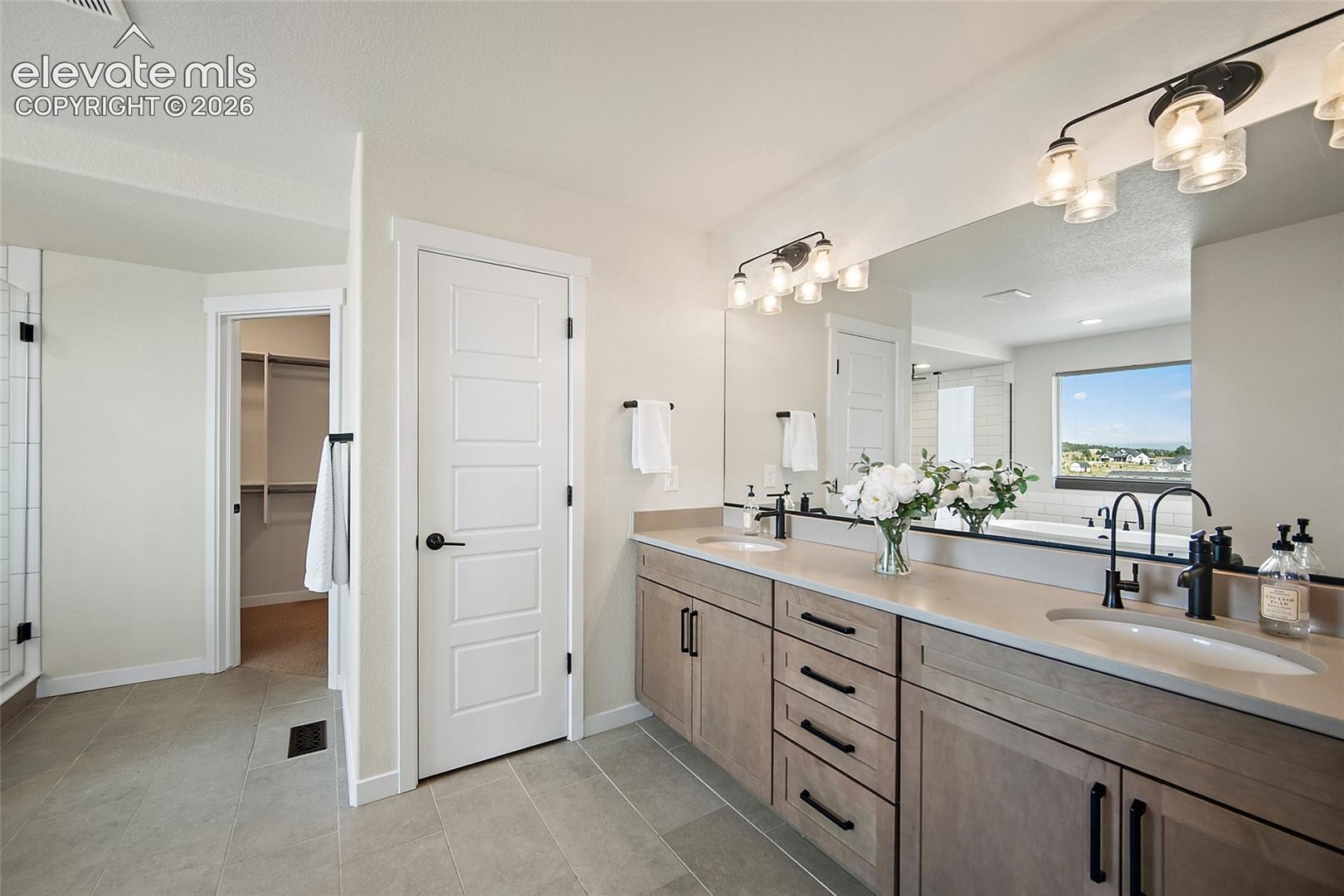 Dual vanity with stone-finish countertops, matte black fixtures, full-width mirror, and overhead lighting